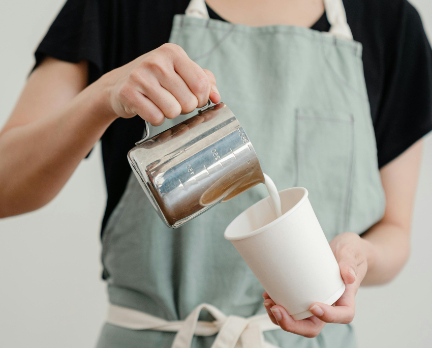 barista in unform apron pouring milk into coffee - benefits of work uniforms
